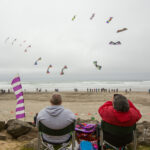 Two people watch kites flying over Rockaway Beach.